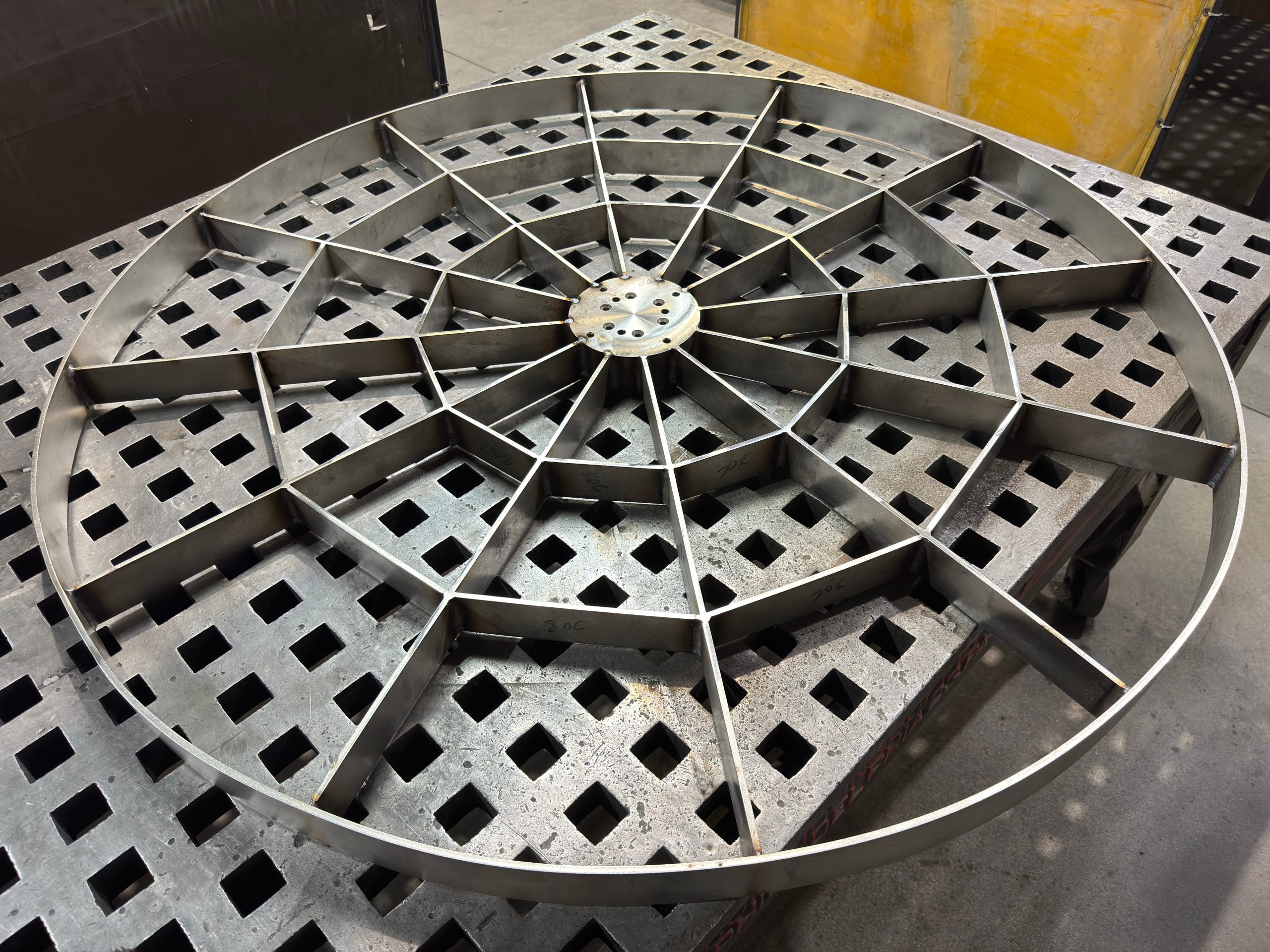 Metal circular lattice frame with a radial spoke pattern on a workshop floor.